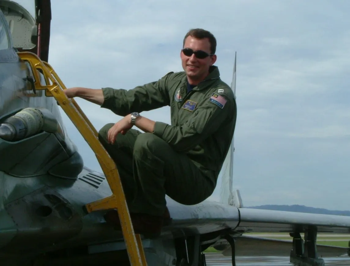 Dr. Monlux seated on a jet wing in a green flight suit